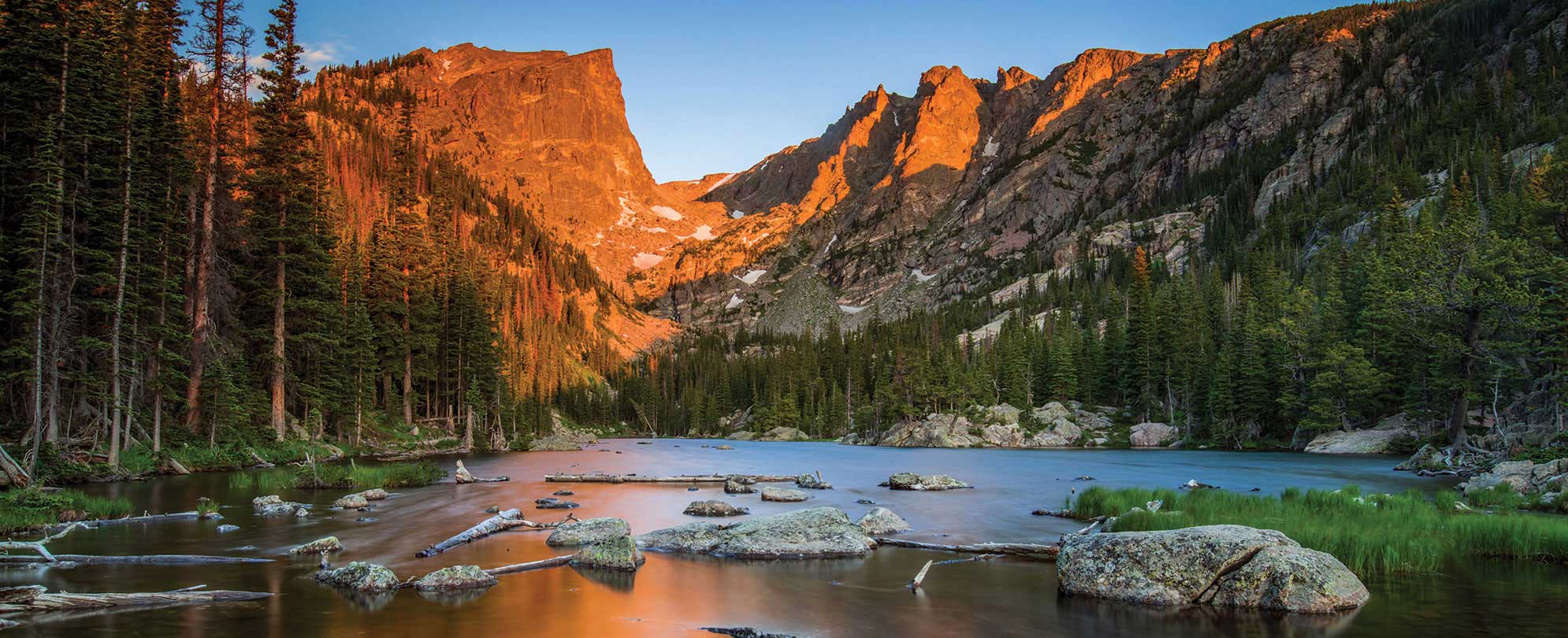 A peaceful creek lined with evergreen trees with the mountains in the background at Rocky Mountain National Park in Colorado