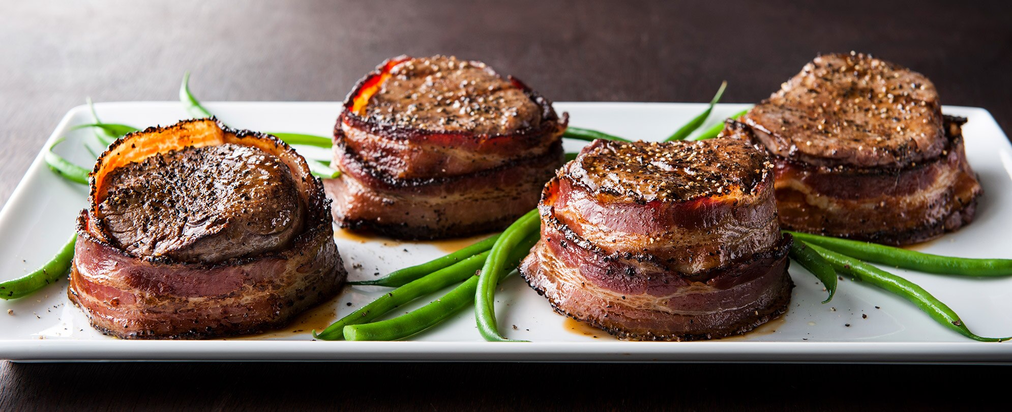 A plate of four bacon wrapped steak medallions with green beans at a restaurant in San Diego, California. 