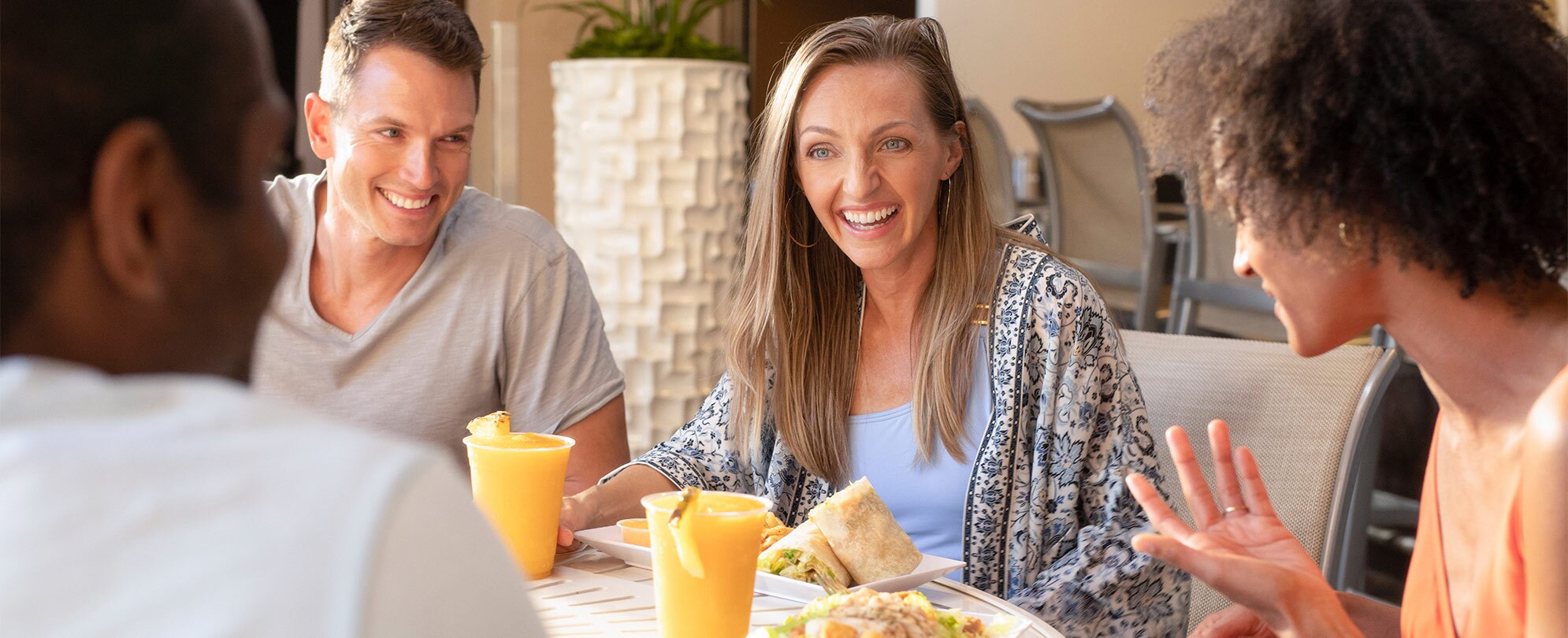 Four adults sit at a table smiling, talking, and enjoying lunch with frozen cocktails.