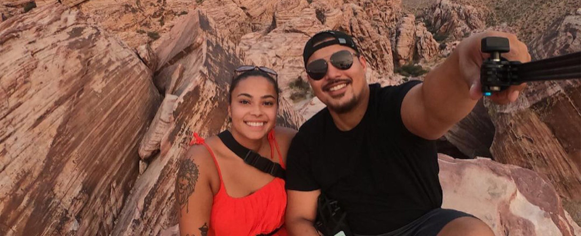 A smiling couple sits on top of a rock as they take a selfie at Red Rock Canyon in Las Vegas, Nevada