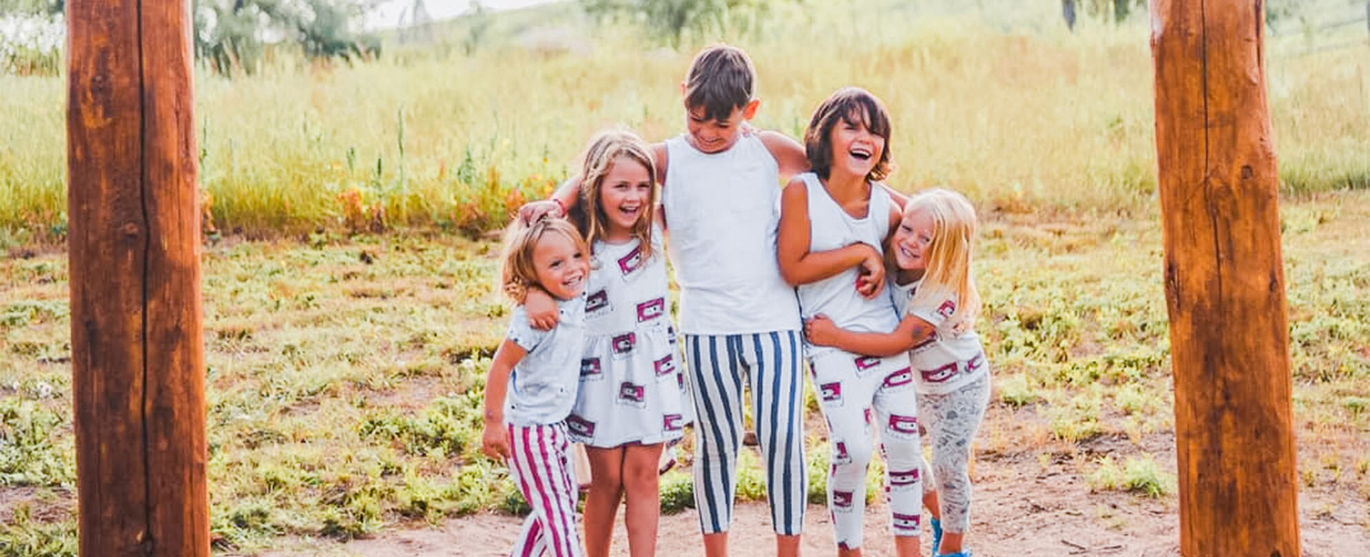 Five young kids dressed in coordinating outfits hug under the Welcome to Colorado sign