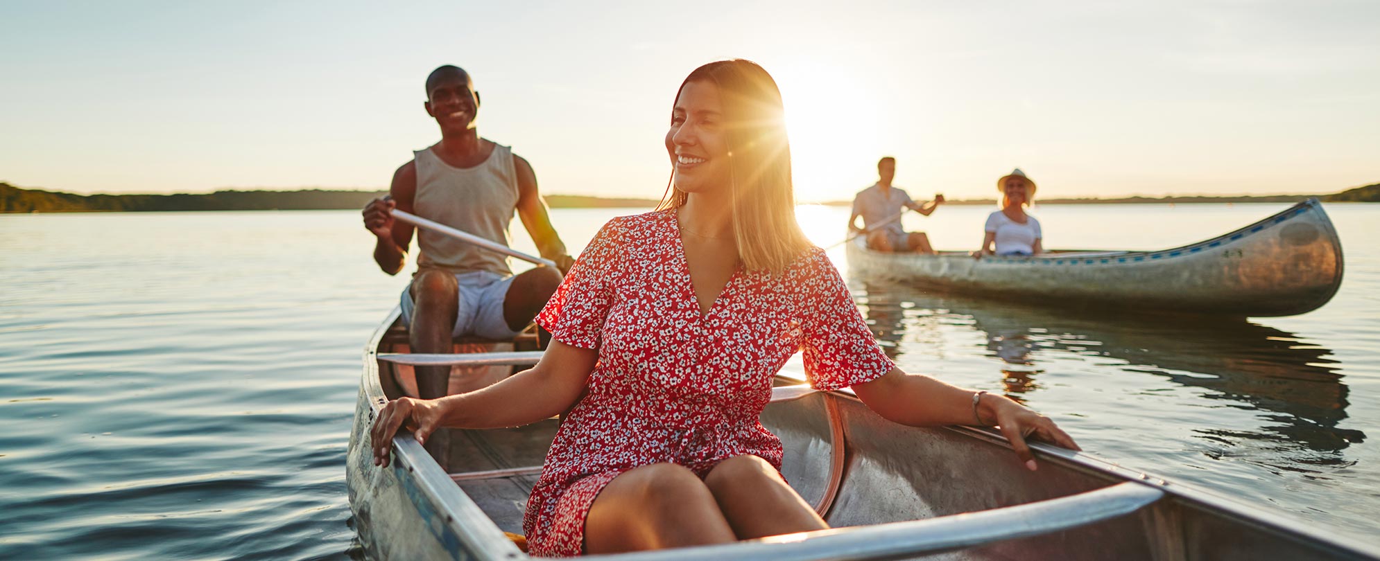 Four friends paddle two canoes around a lake as the sun sets while on vacation